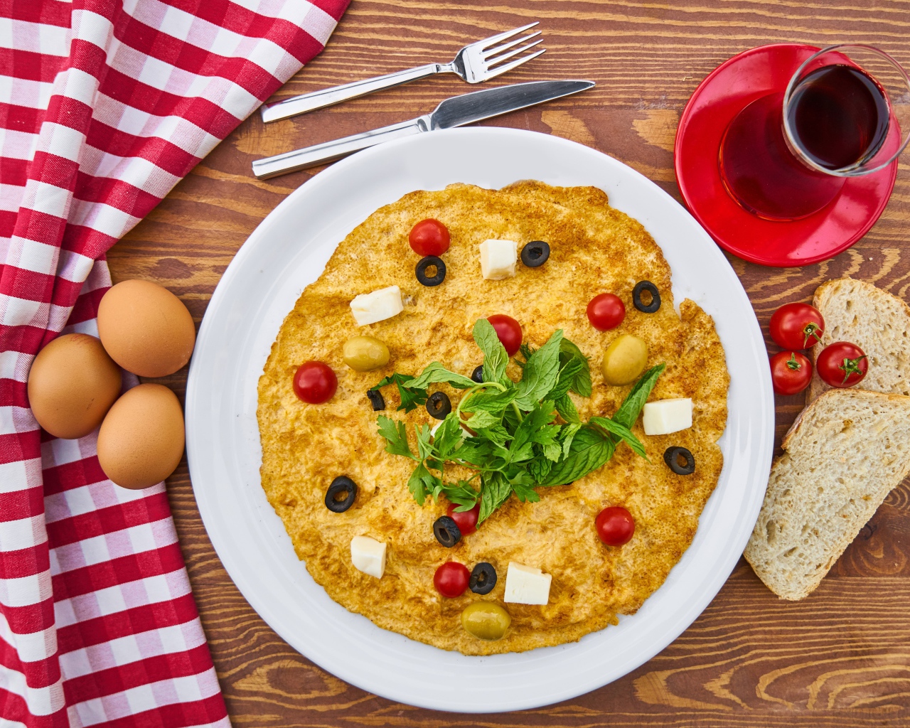 Omelet on the table with tea, tomatoes, eggs and bread