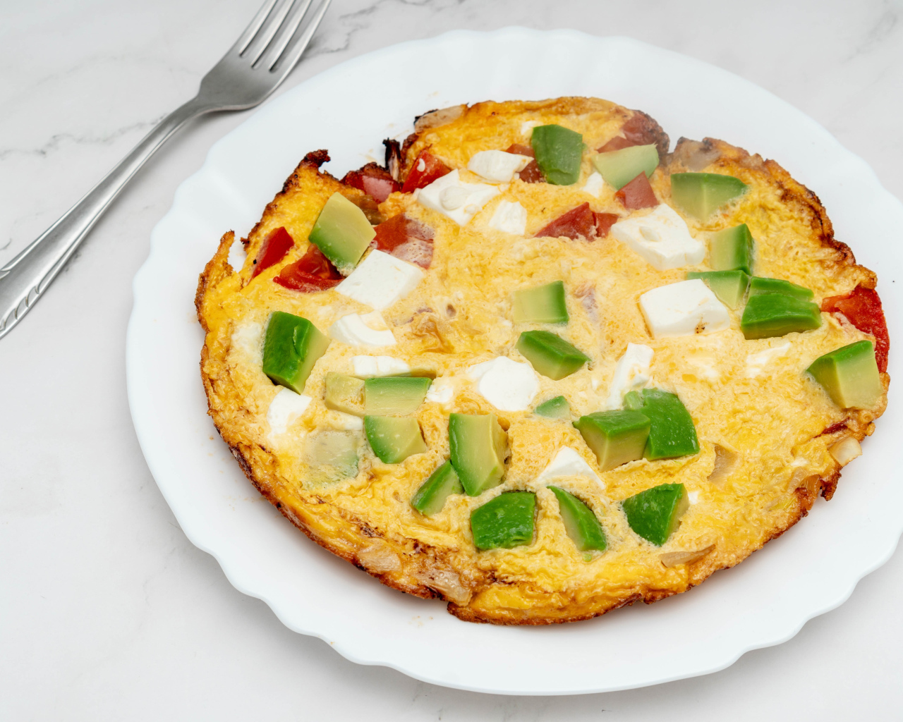 Омлет с авокадо и кусочками помидора на белой тарелке 