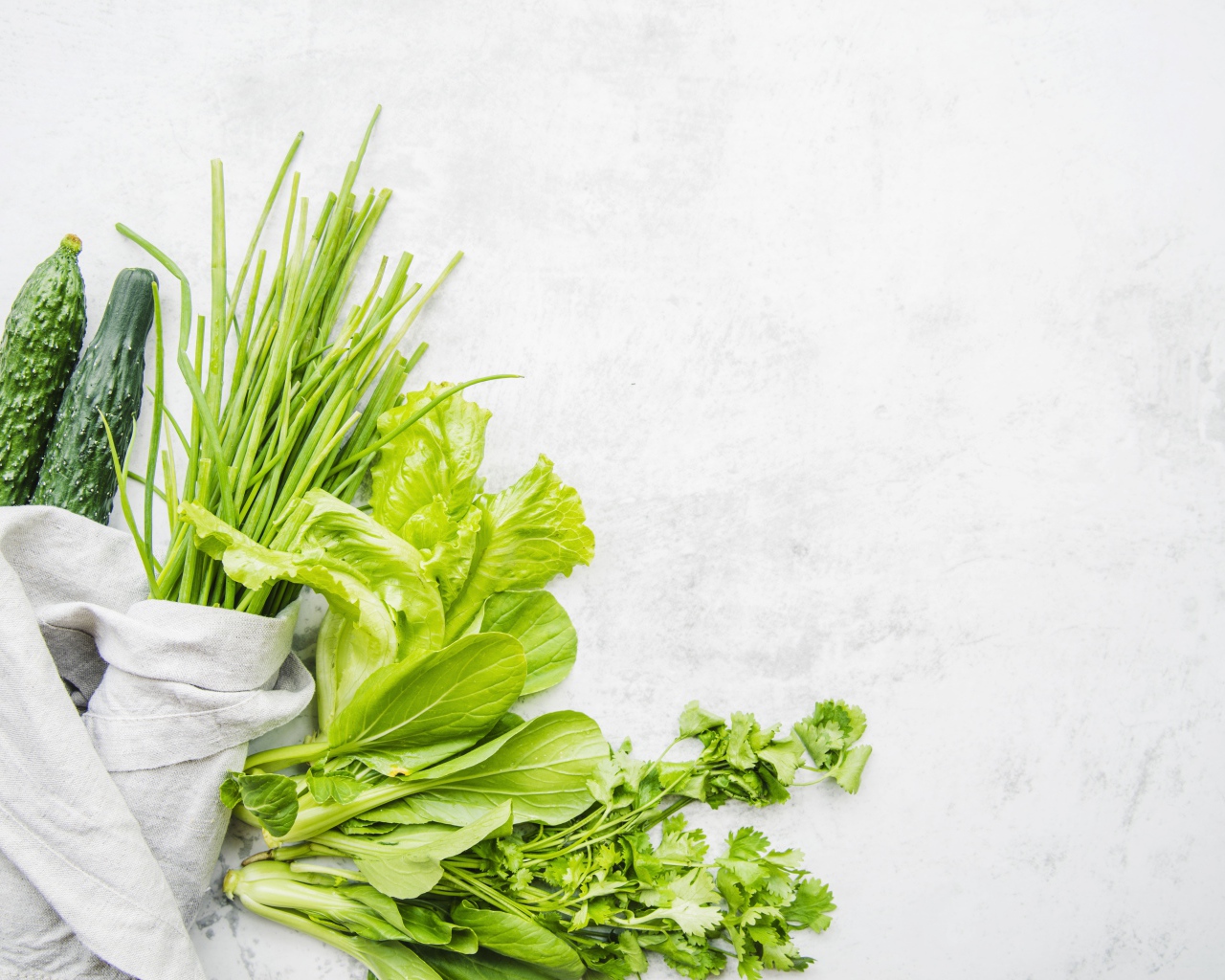 Зелень петрушки и лука, листья салата и свежие огурцы на белом фоне