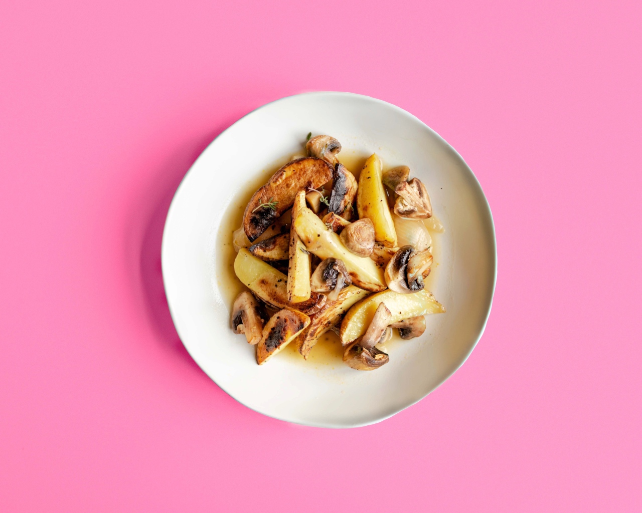 Картофель с грибами в тарелке на розовом фоне 