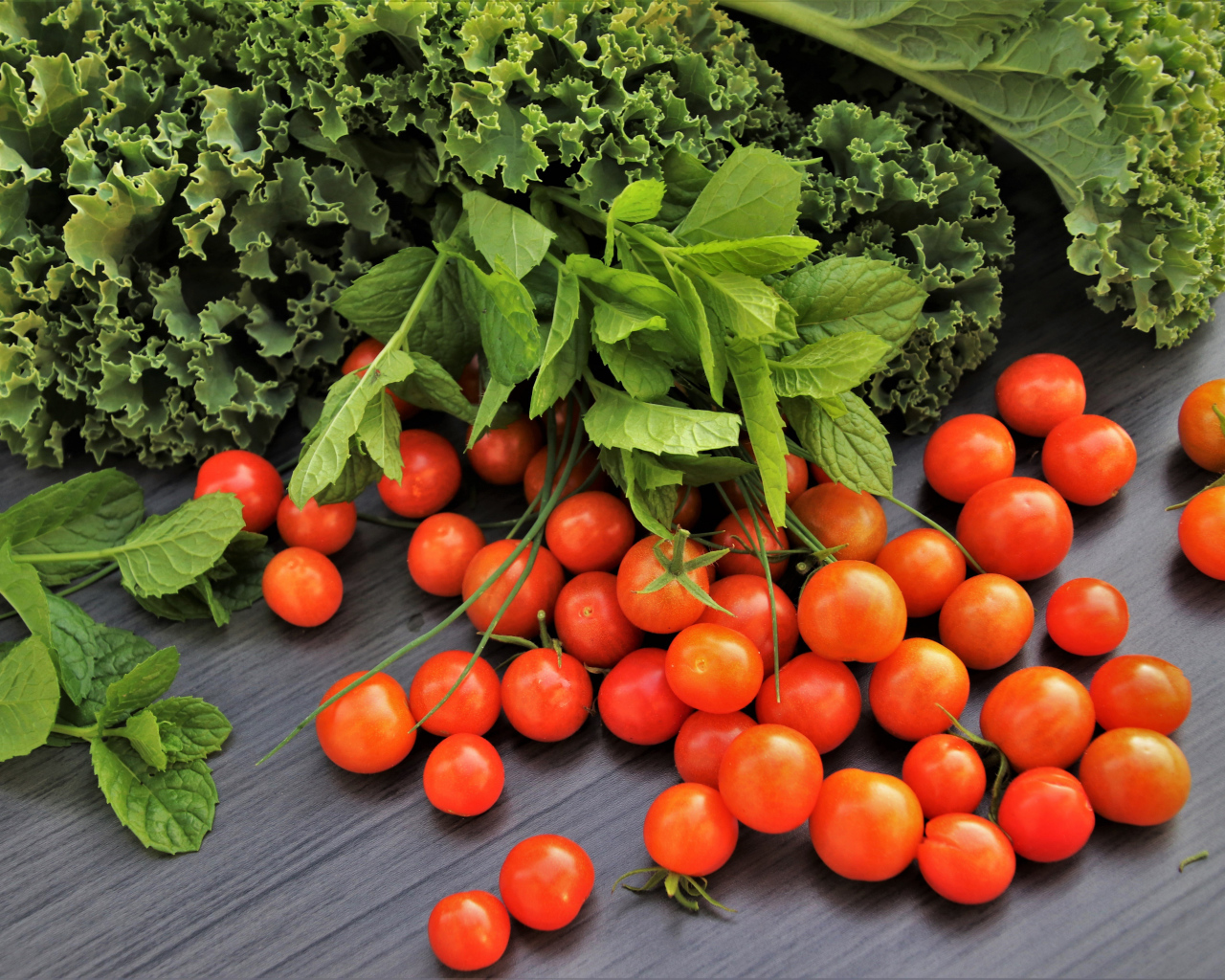 Красные мелкие помидоры на столе с зеленью 