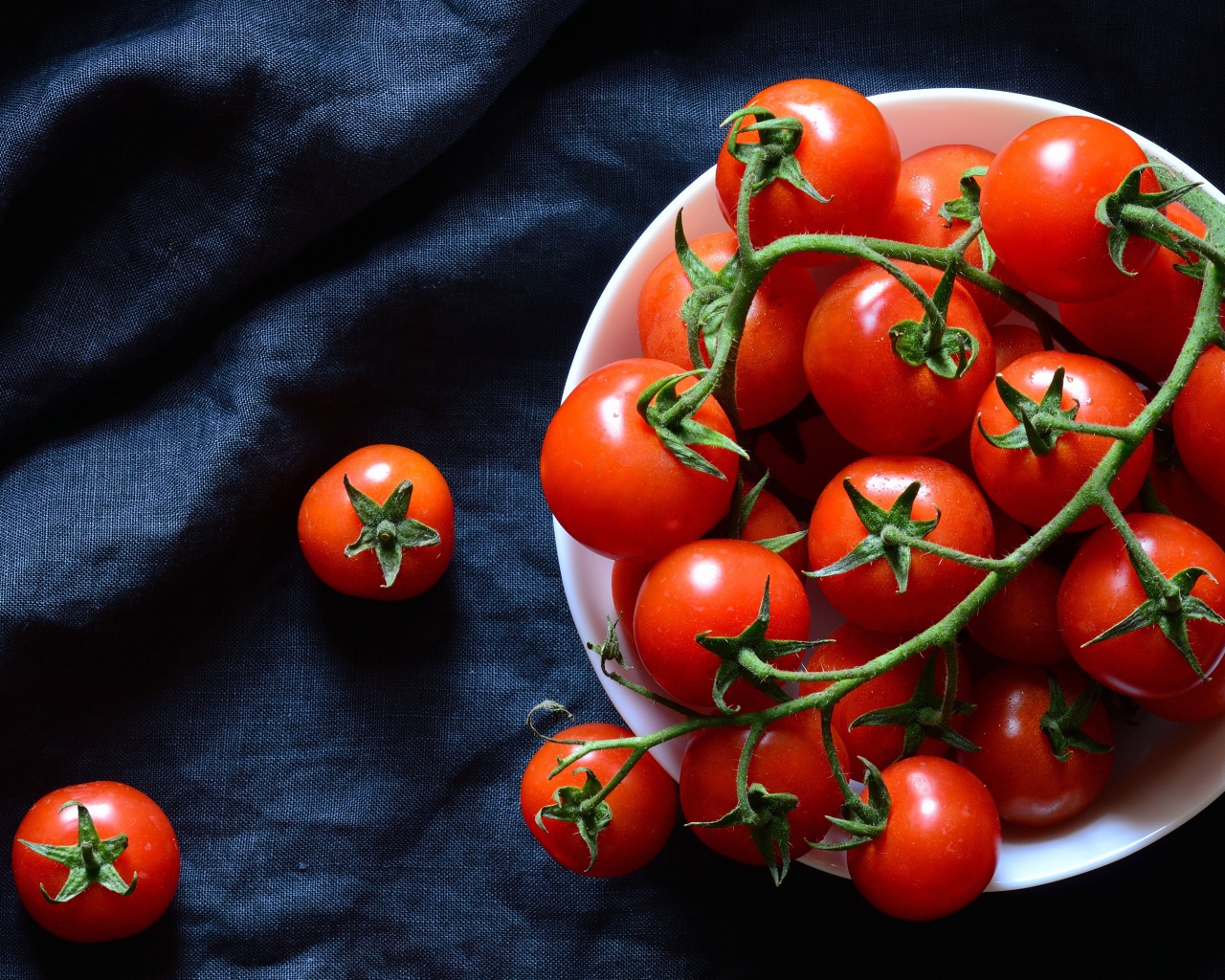 Красные помидоры в белой миске на черном фоне