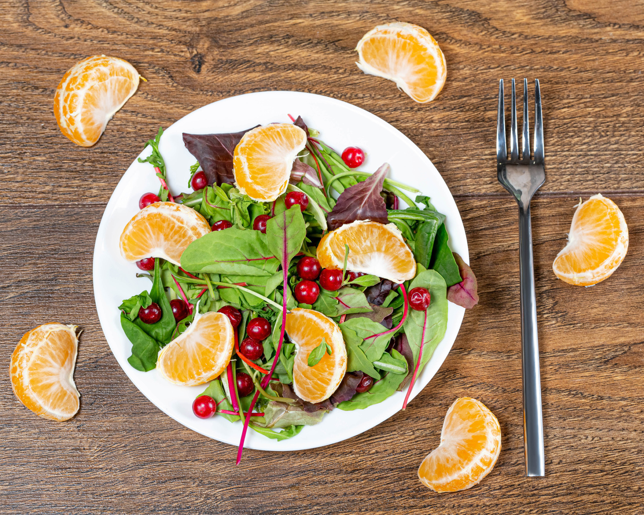 Салат из зелени и мандарина на белой тарелке на столе с вилкой