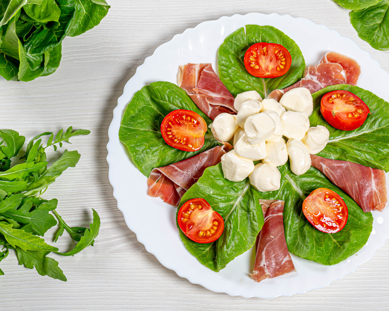 Кусочки ветчины на тарелке с сыром, помидорами и листьями салата
