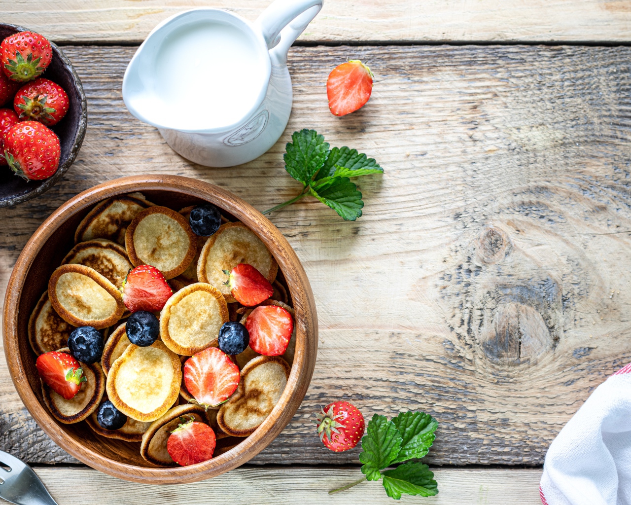 Маленькие оладьи в миске с клубникой и черникой на столе с молоком 