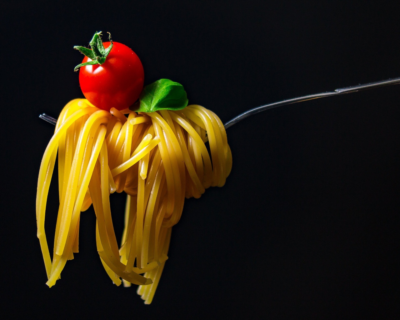 Спагетти с помидором на вилке на черном фоне
