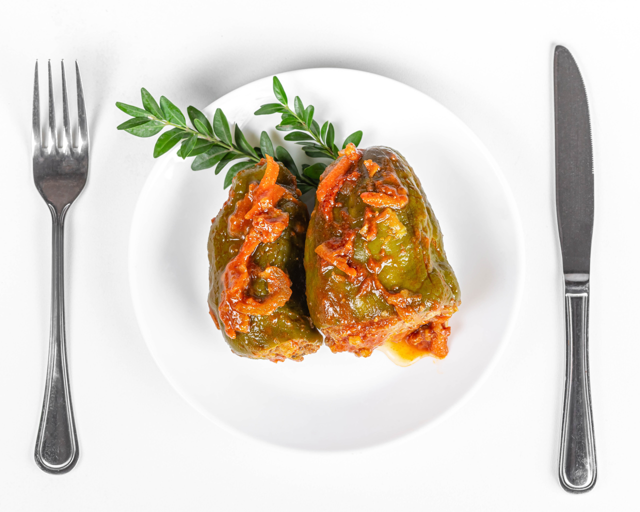 Фаршированный перец на белой тарелке со столовыми приборами