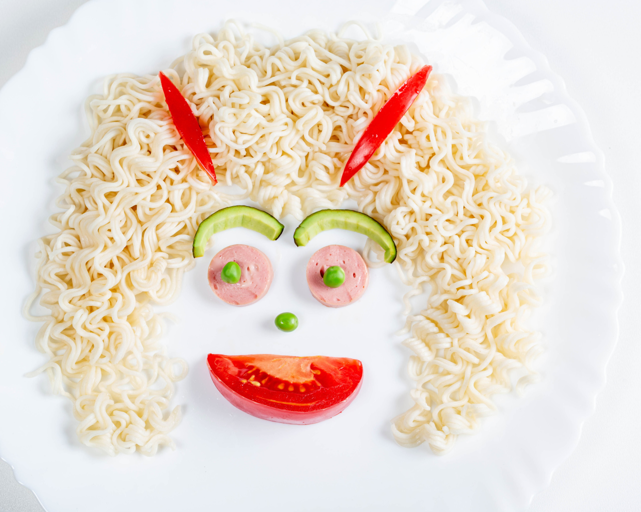 Лицо из вермишели с овощами и колбасой на белой тарелке 