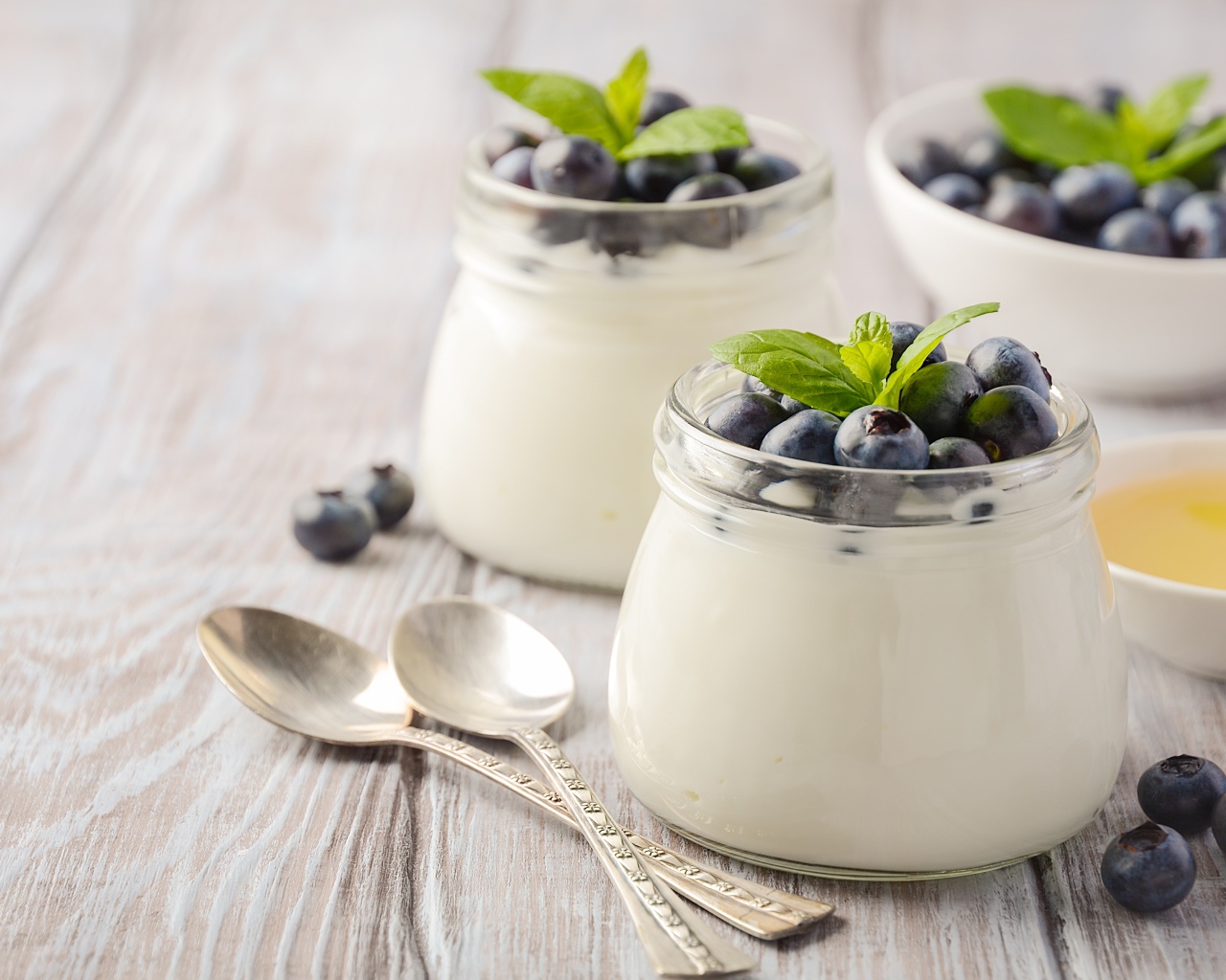 Йогурт в банках с ягодами черники на столе с ложками и медом