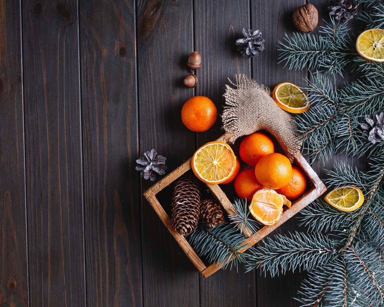 Ящик с мандаринами и шишками на столе с еловыми ветками