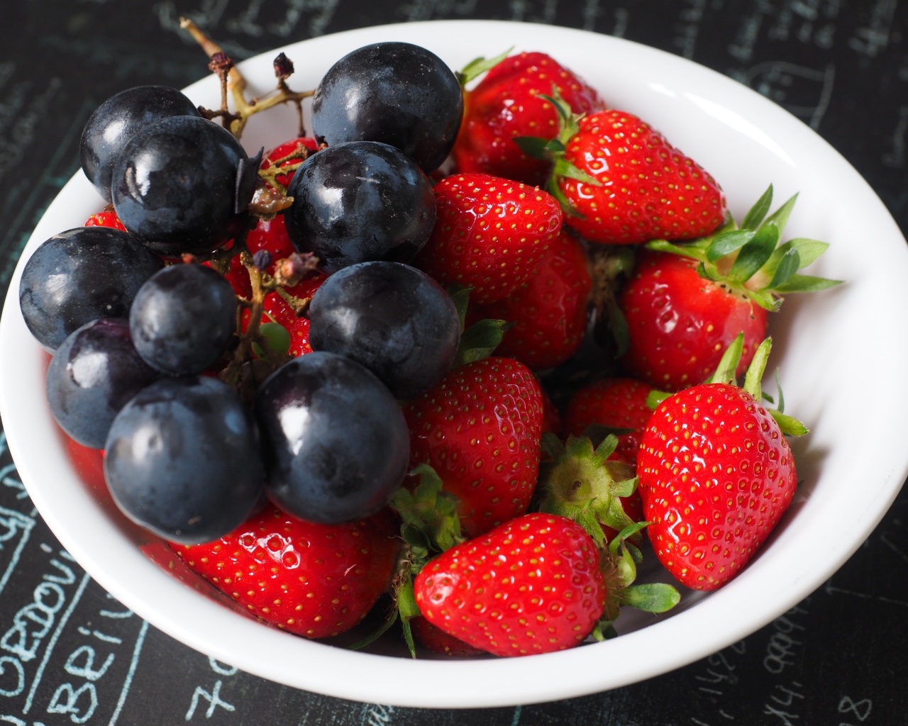 Синий виноград на тарелке с ягодами клубники 