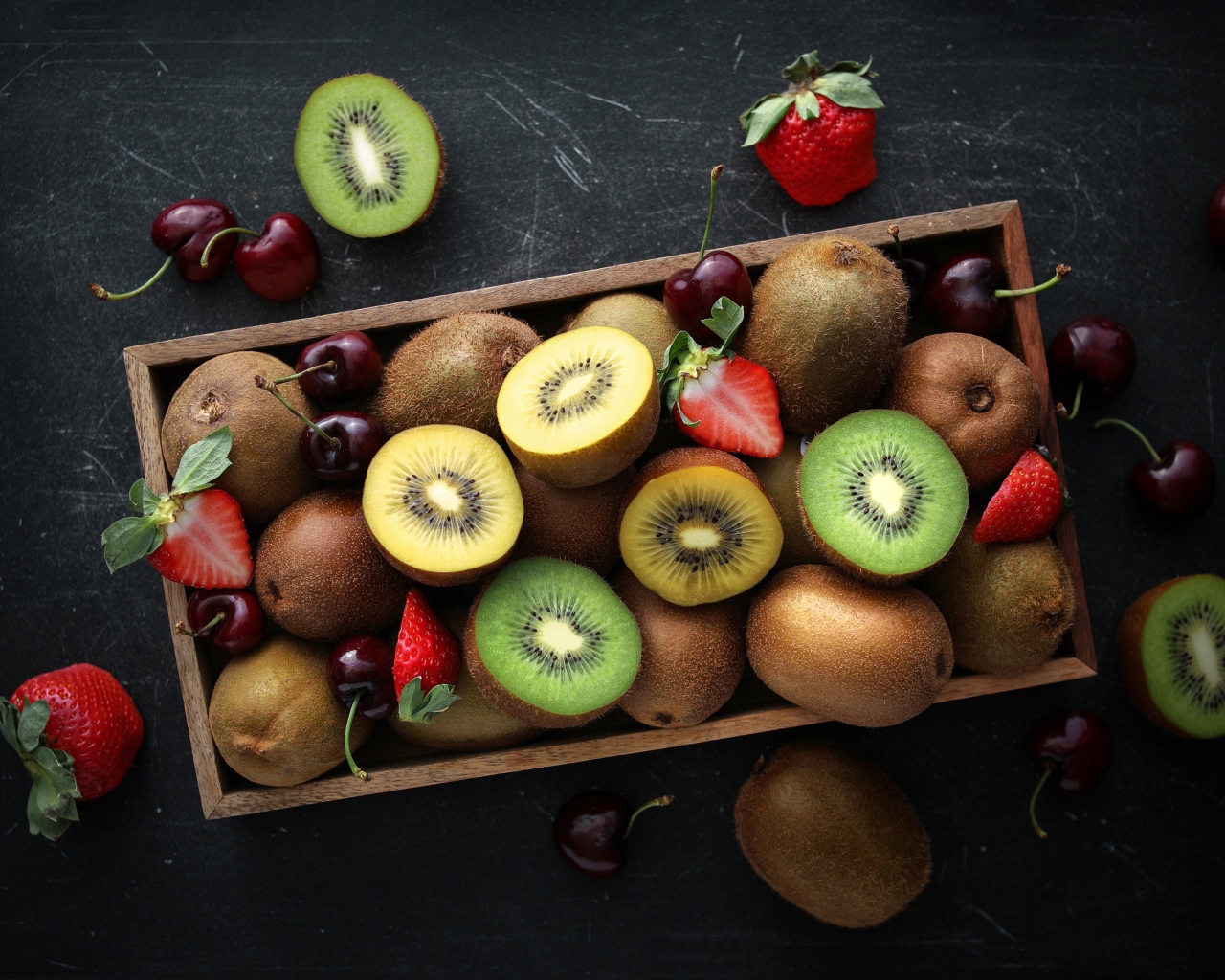 Ящик с киви, клубникой и черешней на столе 