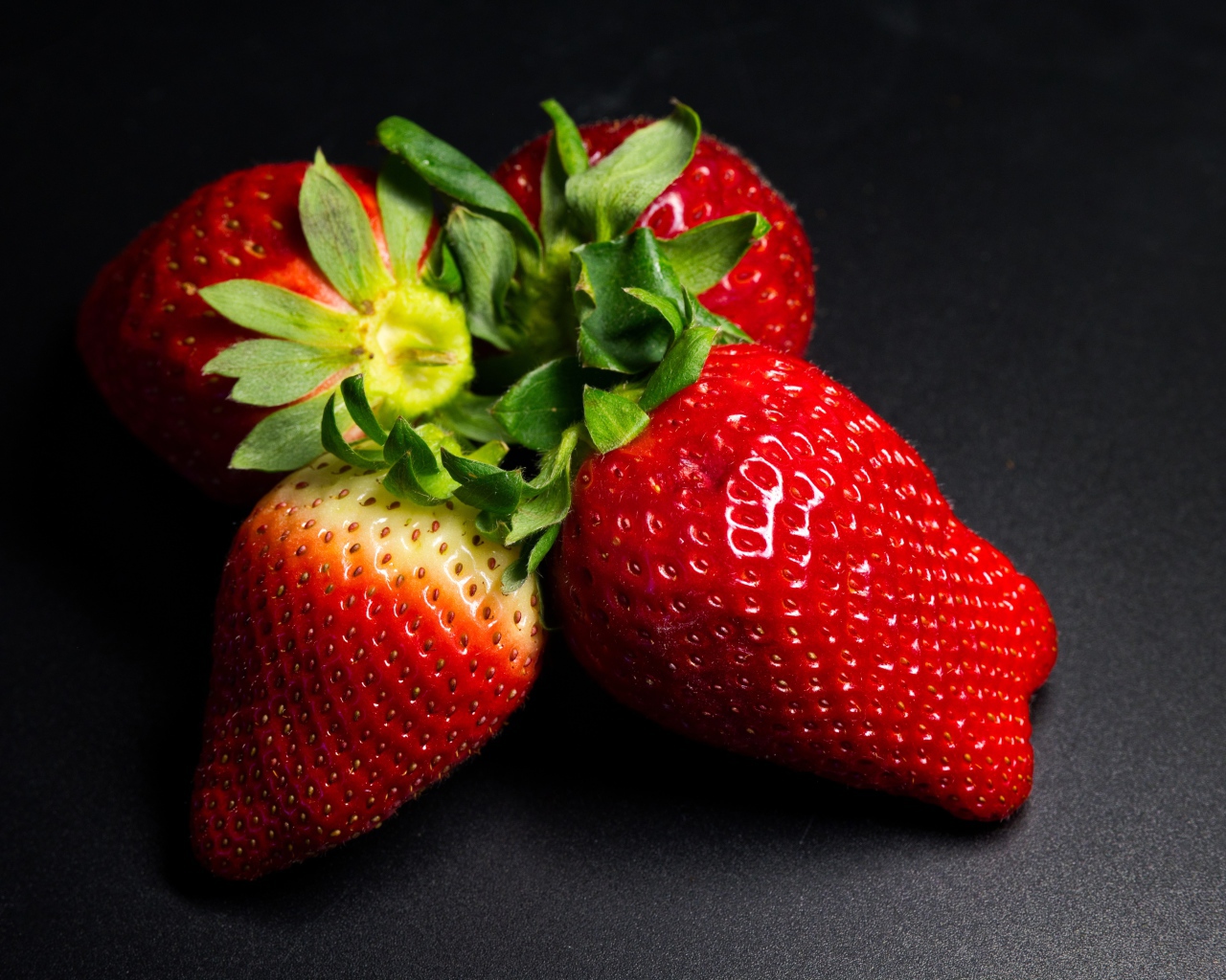 Четыре спелых красных ягоды клубники на черном столе 