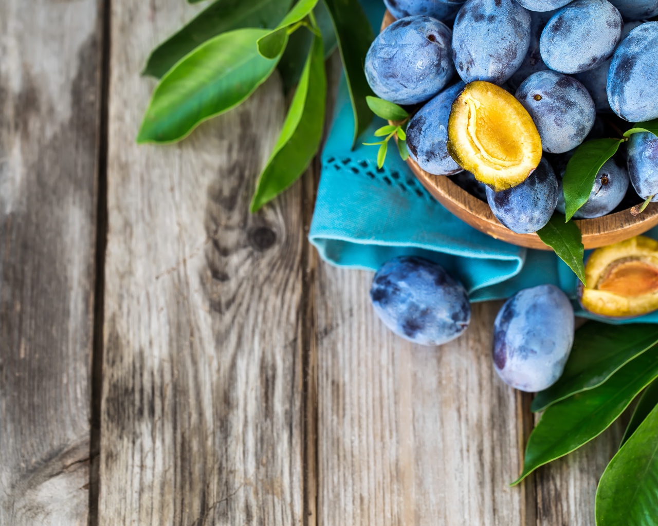Свежие синие сливы с зелеными листьями на столе 