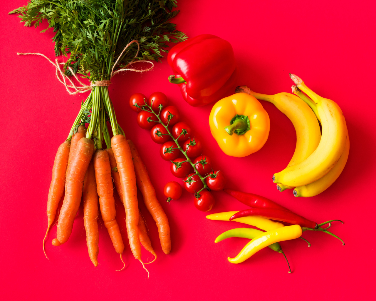 Свежие морковь, помидоры, перец и бананы на красном фоне