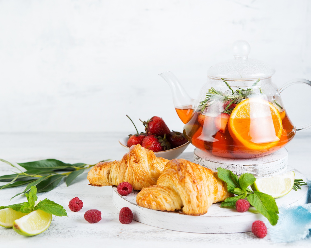 Чайник с лимоном и клубникой на столе с круассанами 