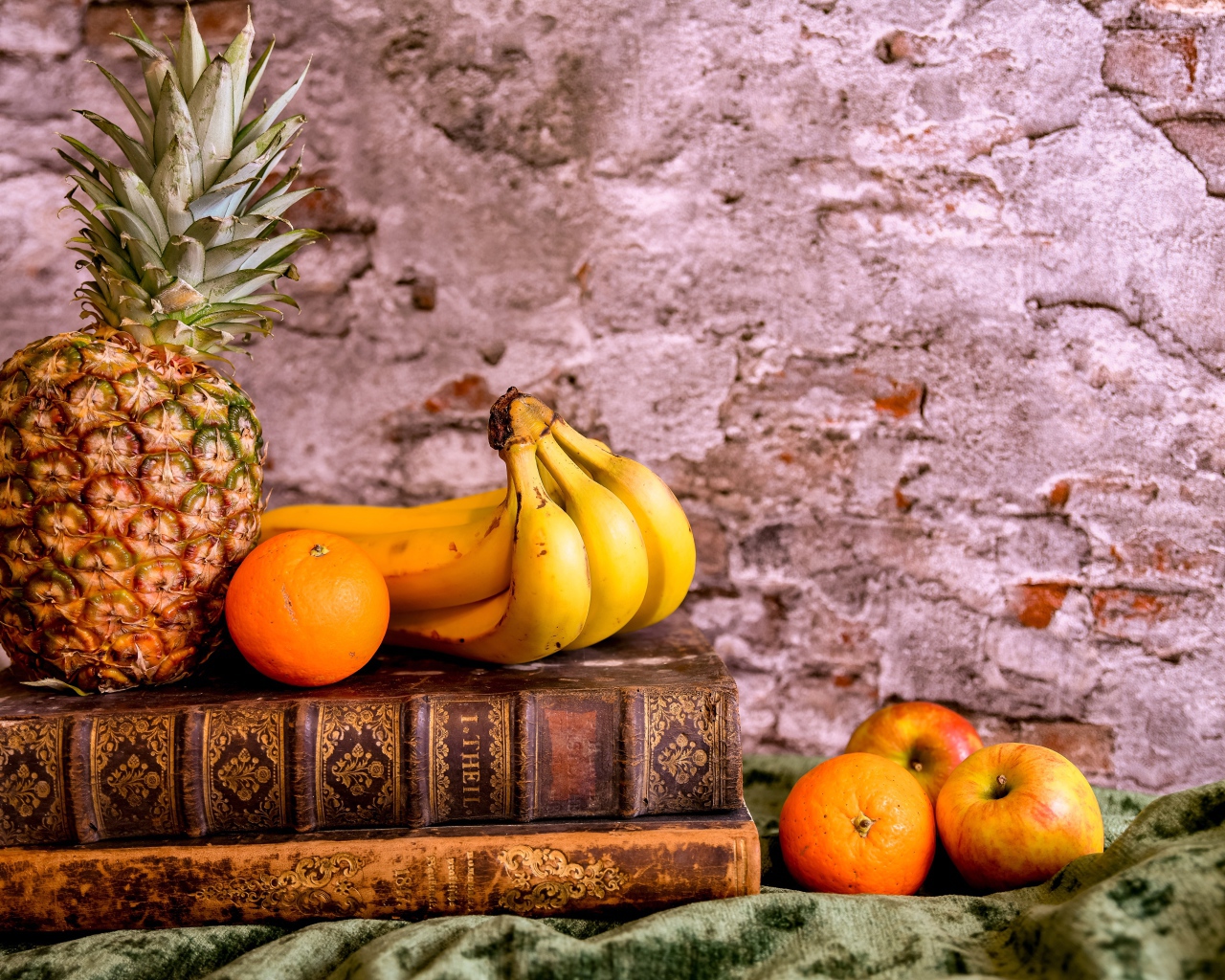 Ананас, бананы, апельсин и яблоки лежат на столе с книгами