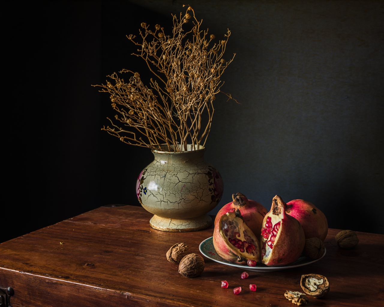 Красный гранат на столе с грецкими орехами и сухой веткой в вазе