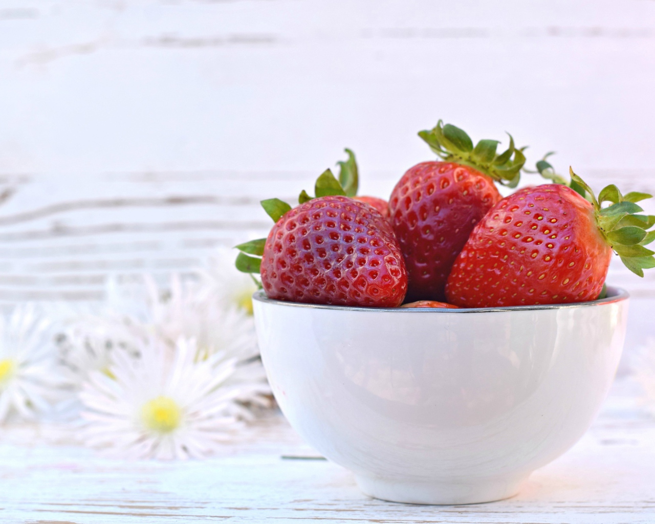 Спелая клубника в белой миске на столе с ромашками