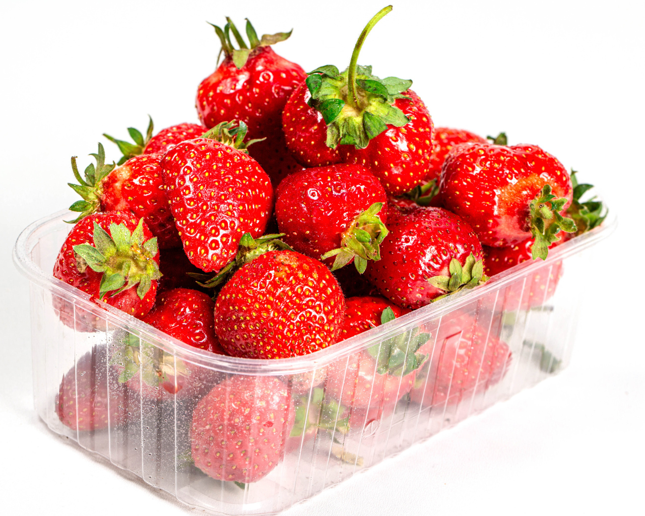 Спелая вкусная клубника в пластиковом контейнере на белом фоне