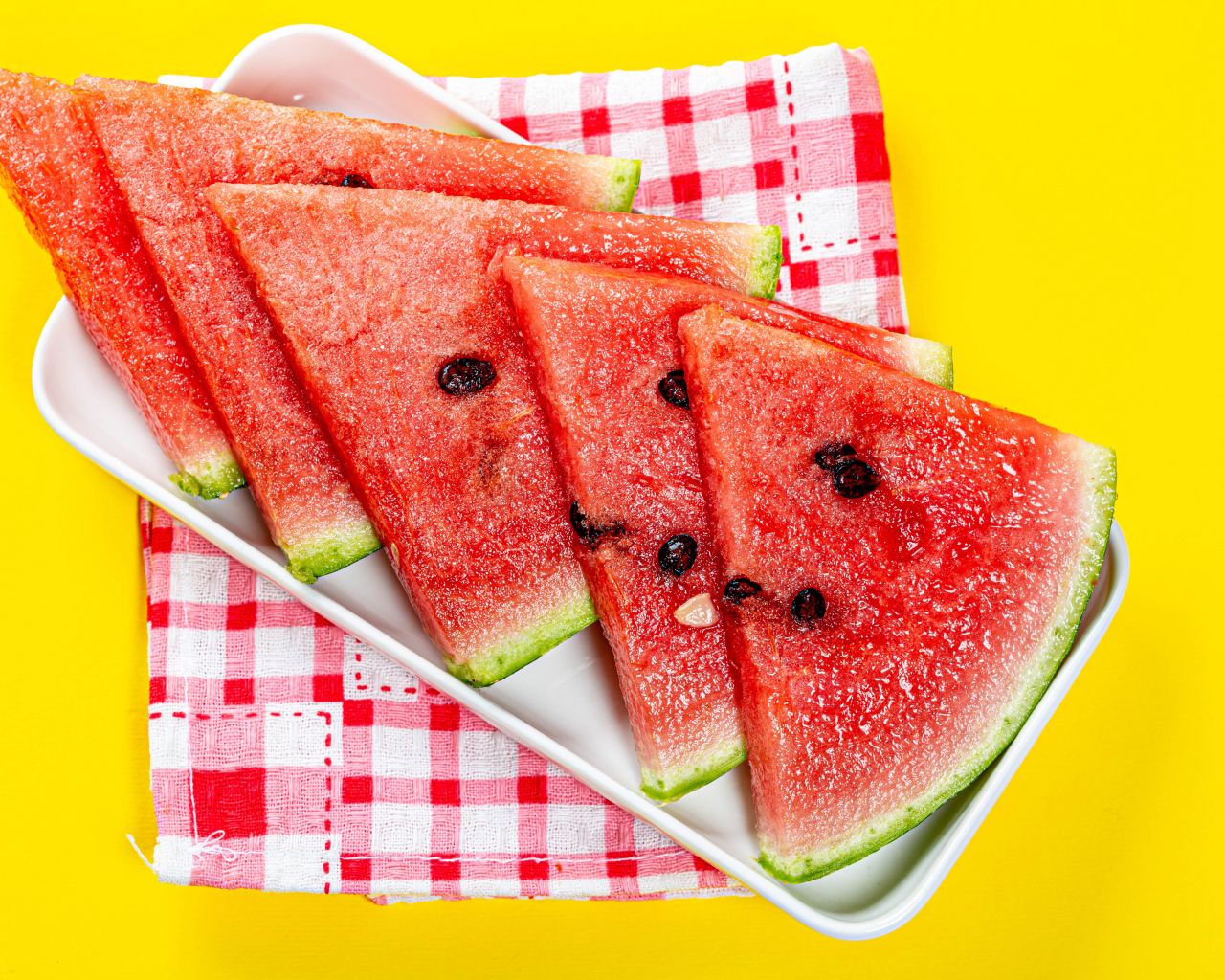 Кусочки сочного арбуза в тарелке на желтом столе