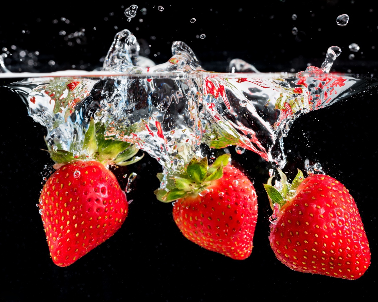 Три ягоды клубники в воде на черном фоне