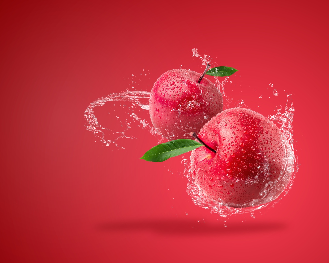 Два яблока в брызгах воды на красном фоне