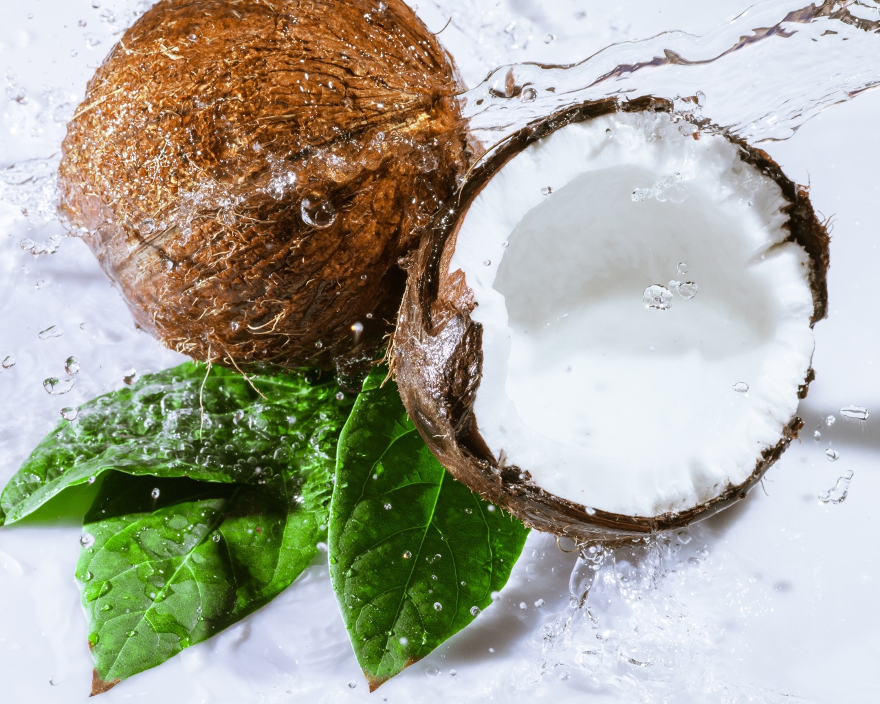 Два кокоса в брызгах воды на белом фоне