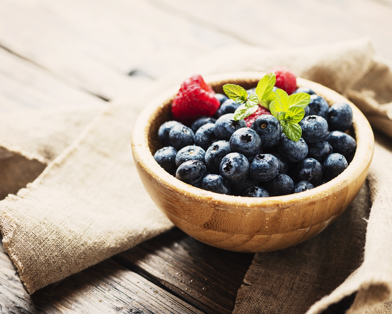 Мокрые ягоды черники в деревянной миске с малиной 