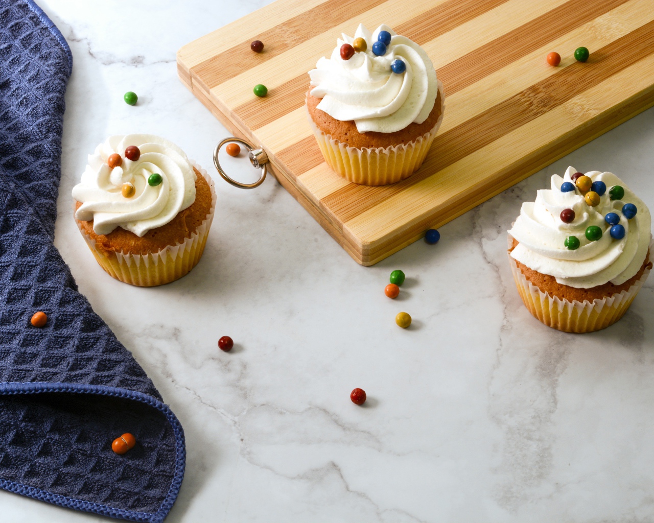 Кексы с кремом и разноцветными шариками на столе с доской