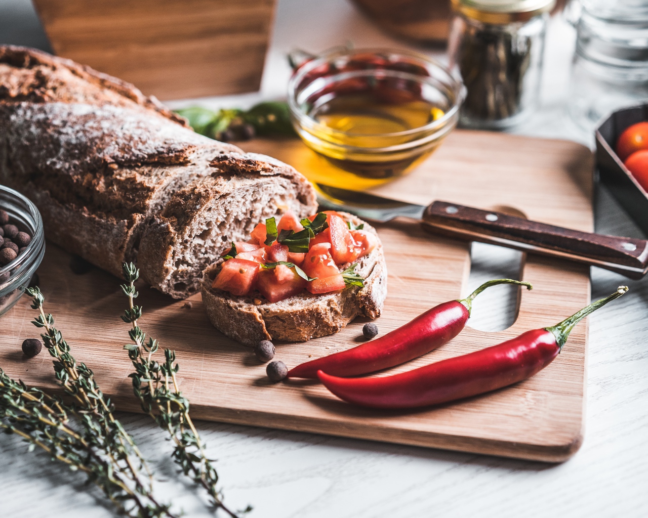 Батон с помидорами и красным перцем на столе с маслом