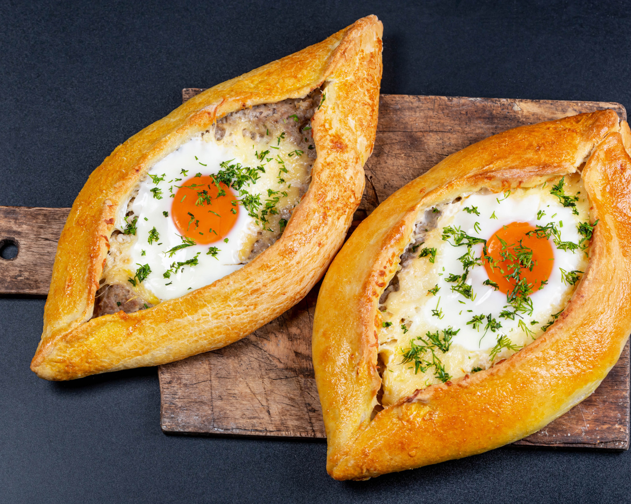 Два больших свежих хачапури с яйцом на доске