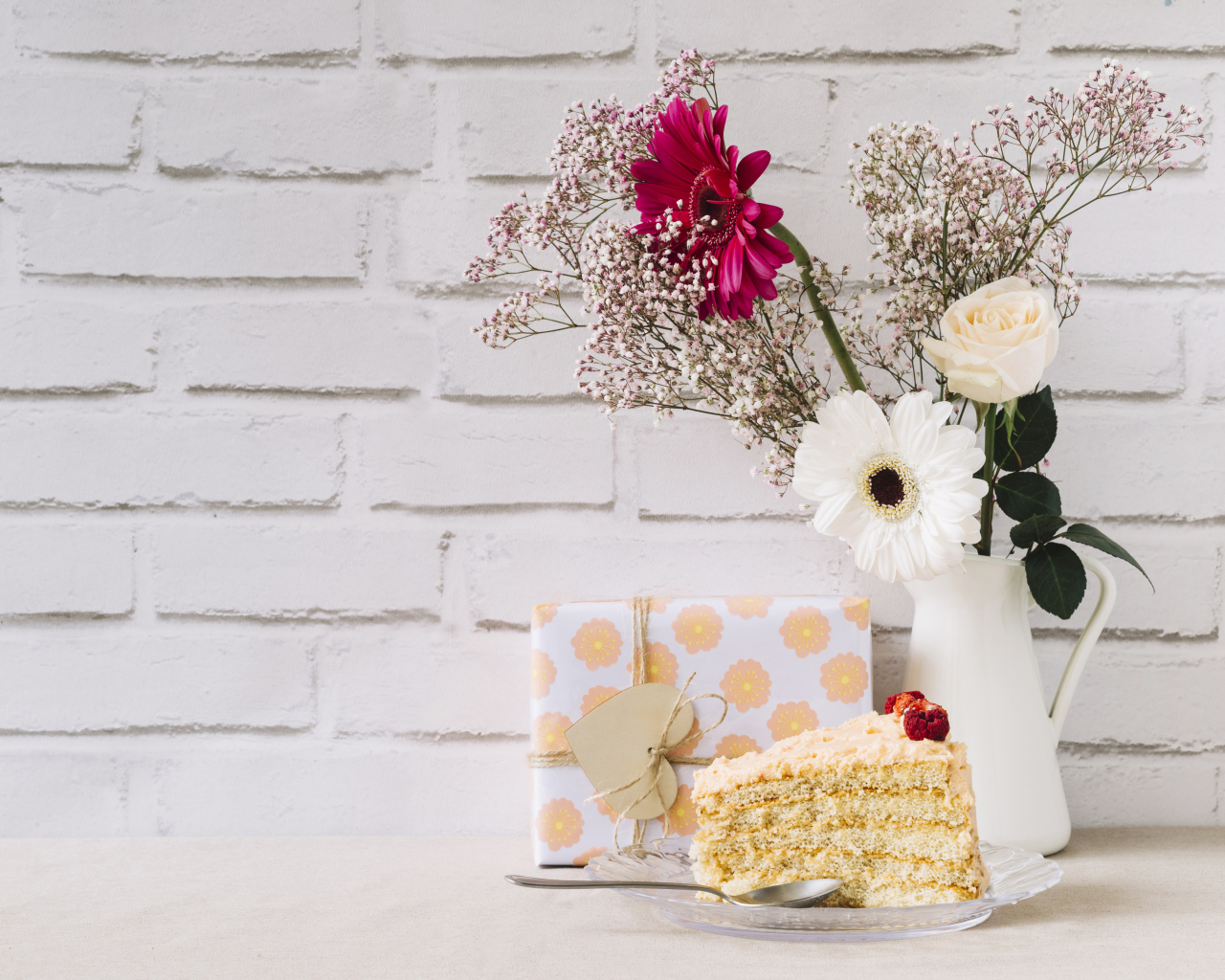 Кусок торта, подарок и букет на столе на фоне стены 