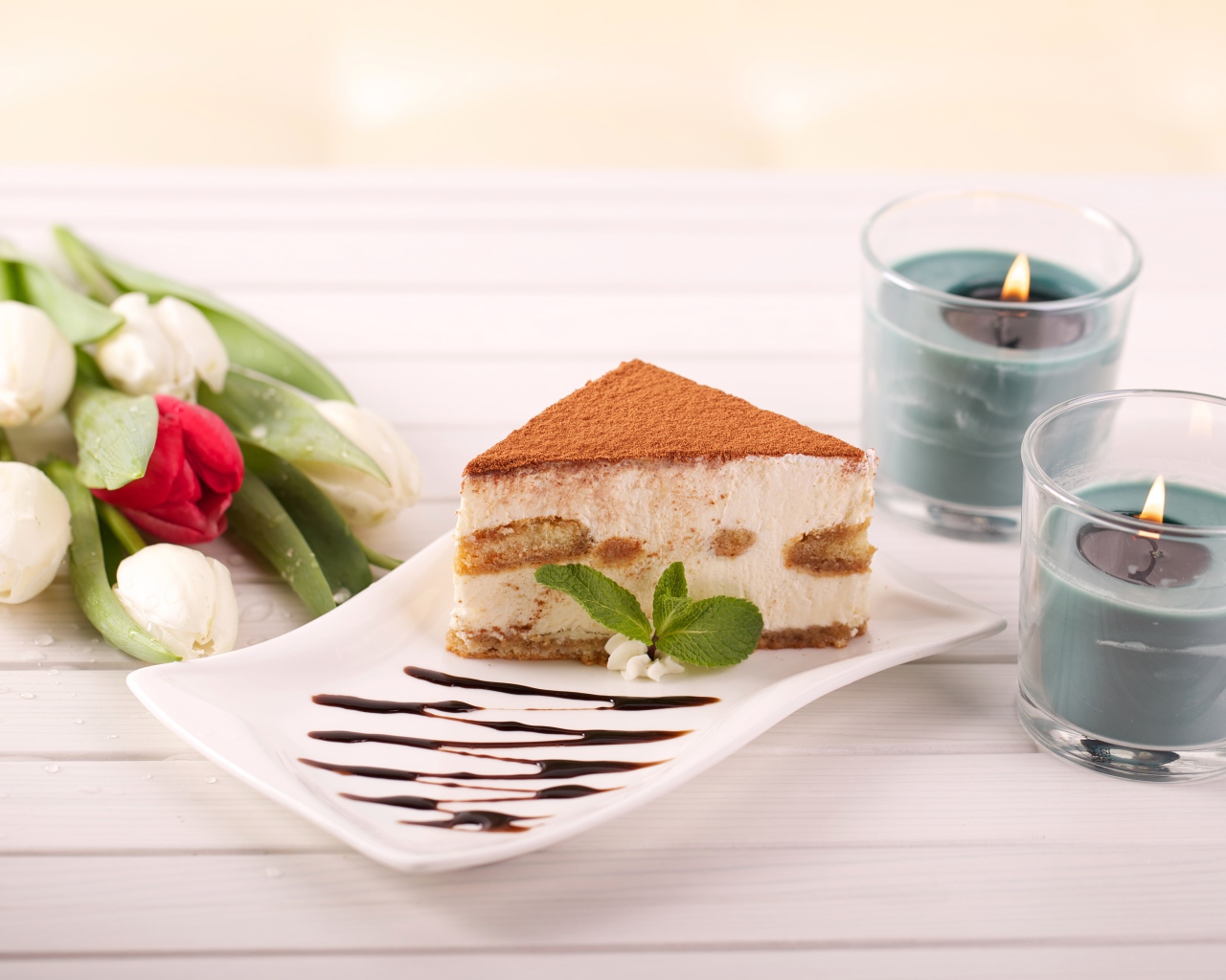 Кусок тирамису на столе с зажженными свечами и букетом тюльпанов