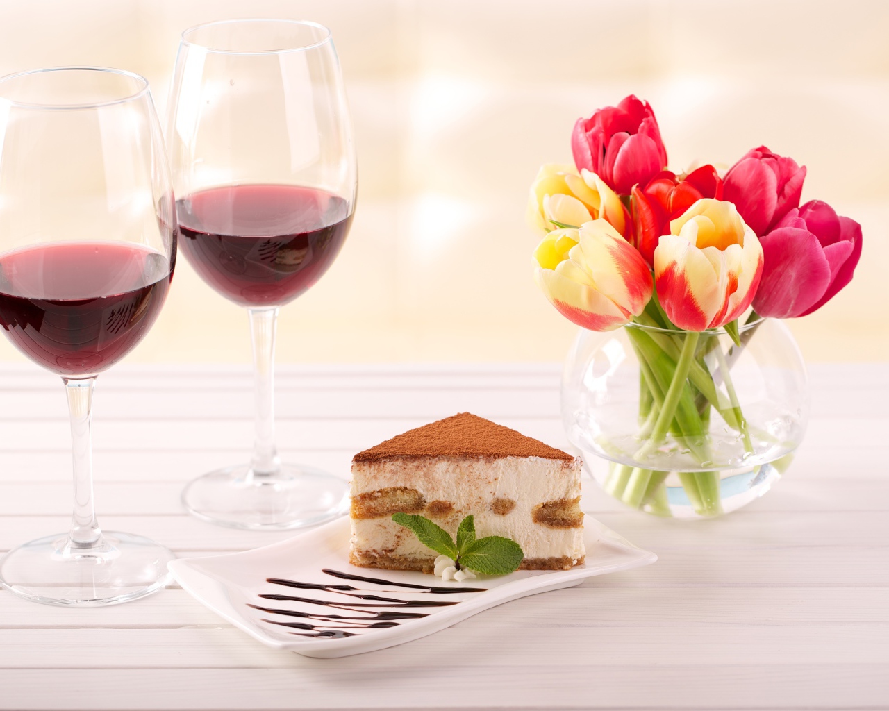 Кусок  тирамису на столе с бокалами вина и букетом тюльпанов