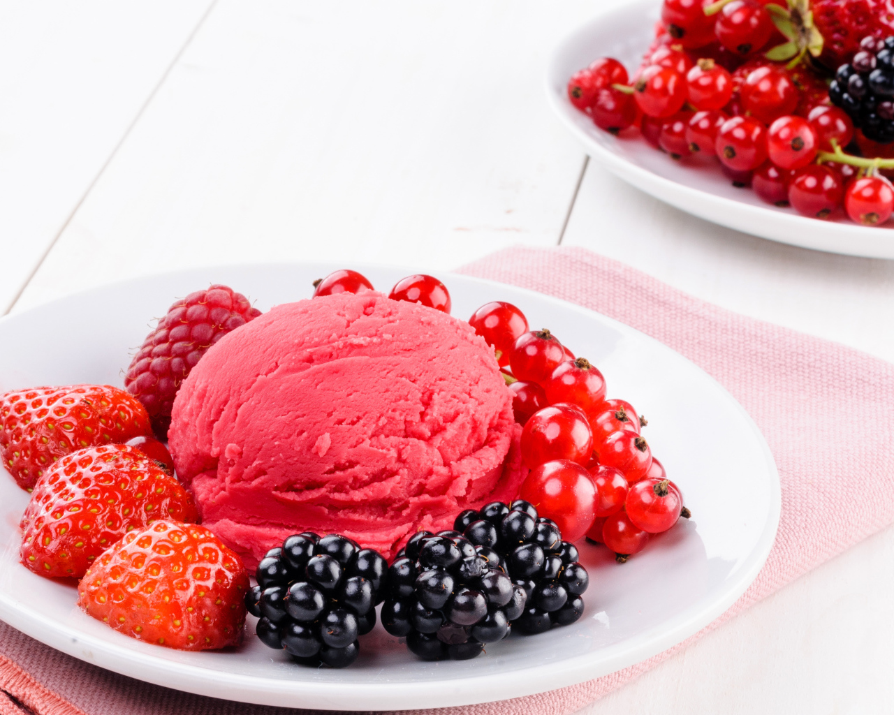 Шарик фруктового мороженого с ягодами на белой тарелке