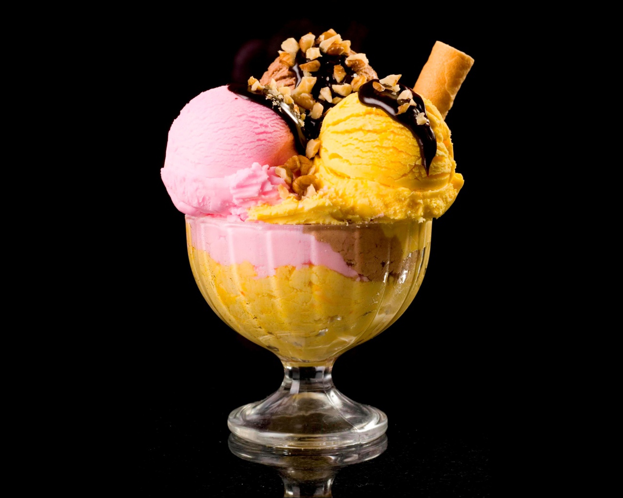 Шарики фруктового мороженого в креманке с орехами и шоколадом на черном фоне