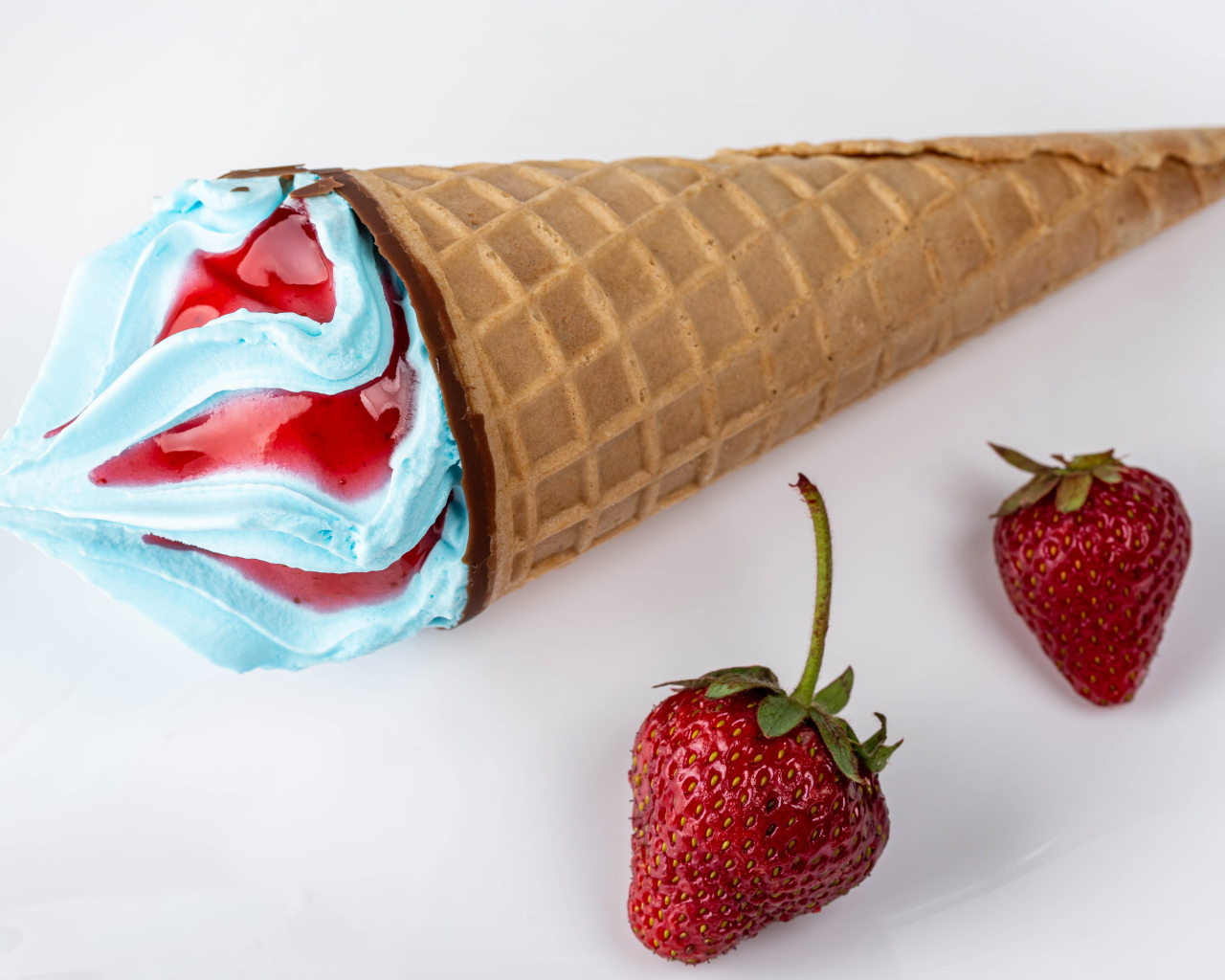 Рожок с голубым мороженым на сером фоне с клубникой 