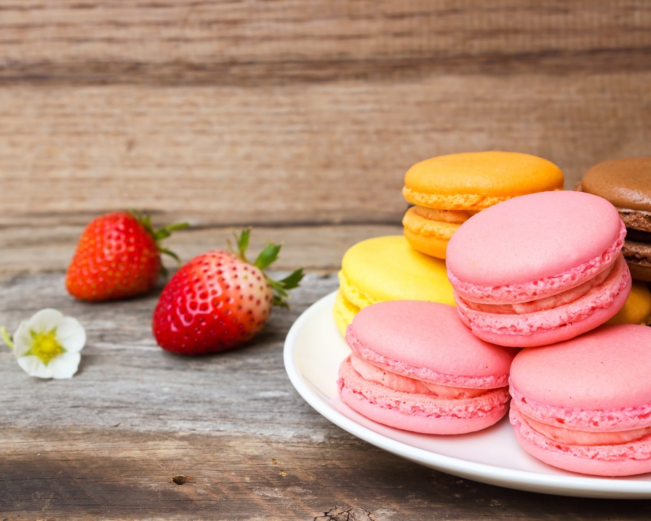 Разноцветный десерт макарун на белой тарелке на столе с клубникой