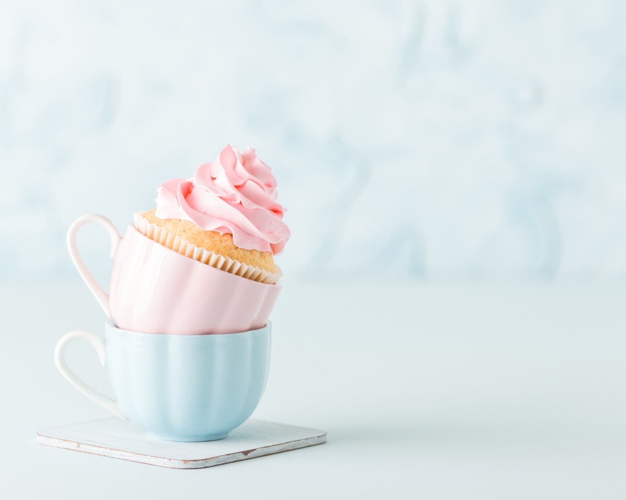 Кекс с розовым кремом с чашками на столе 