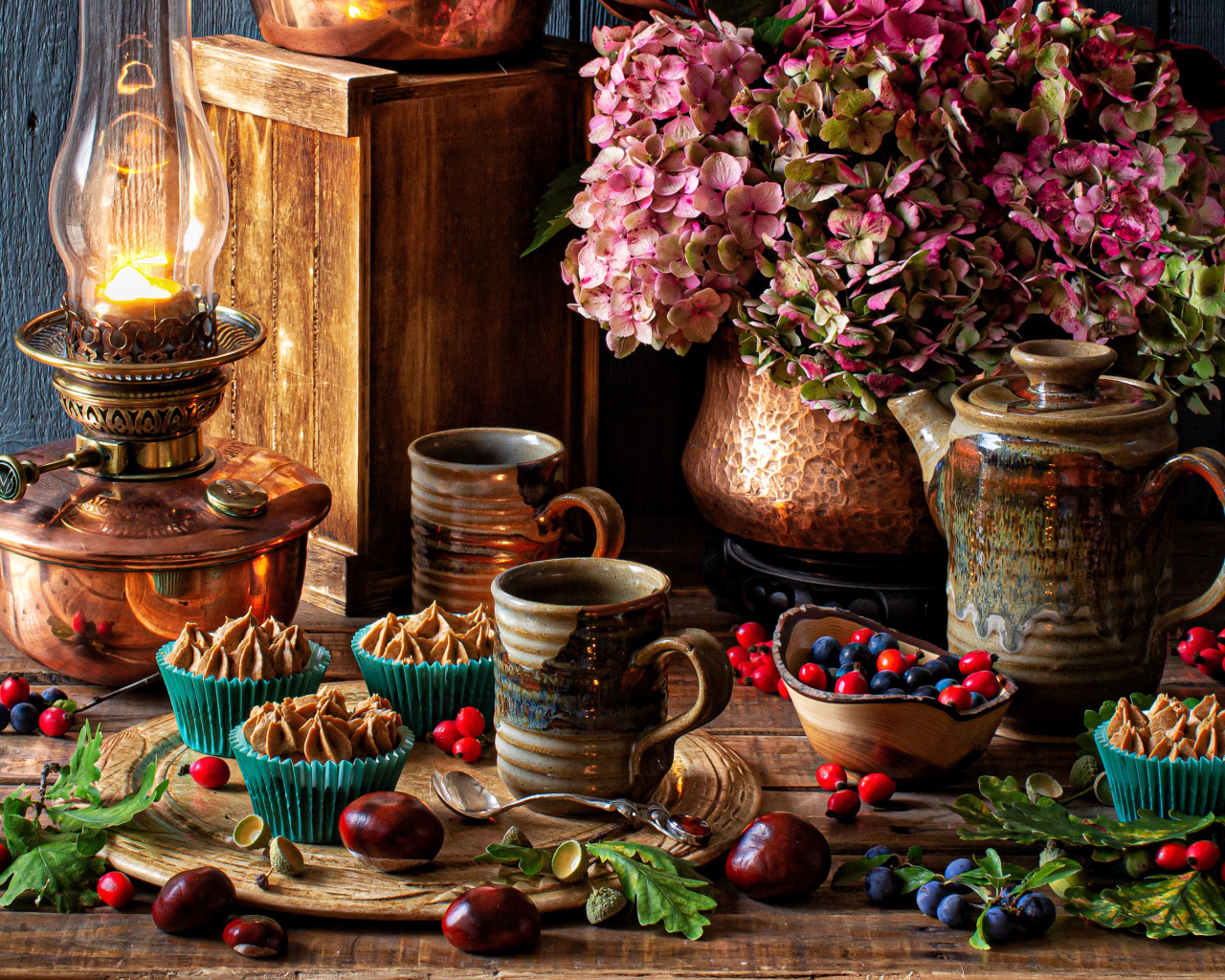 Кексы с кремом на столе с ягодами, цветами и лампой 