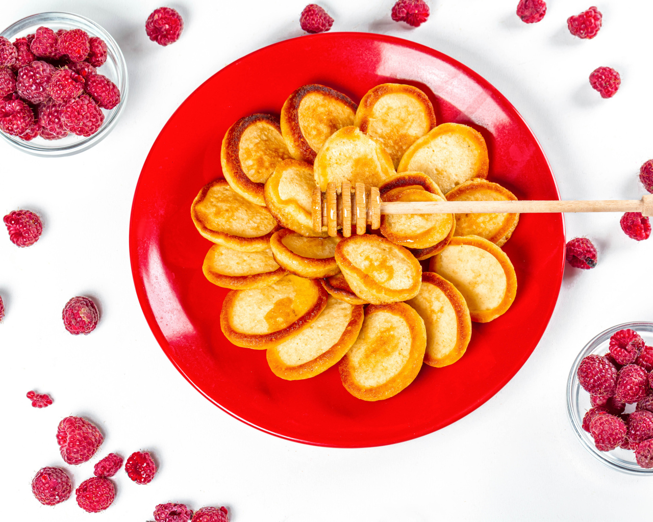 Оладьи на красной с медом на красной тарелке на столе с ягодами малины