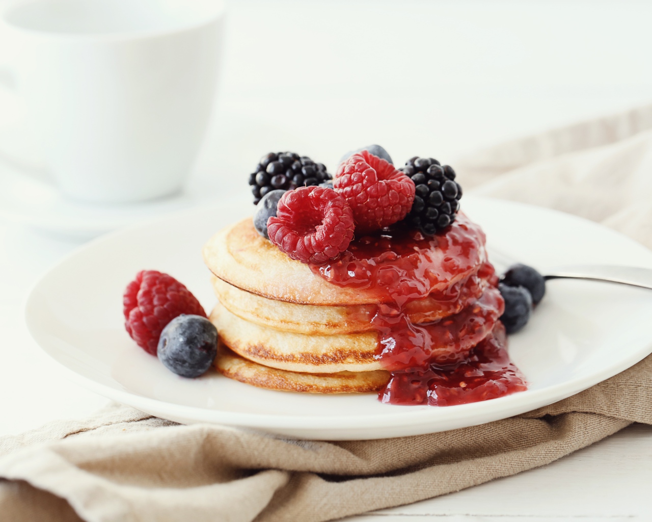 Оладьи на большой белой тарелке с джемом и ягодами 
