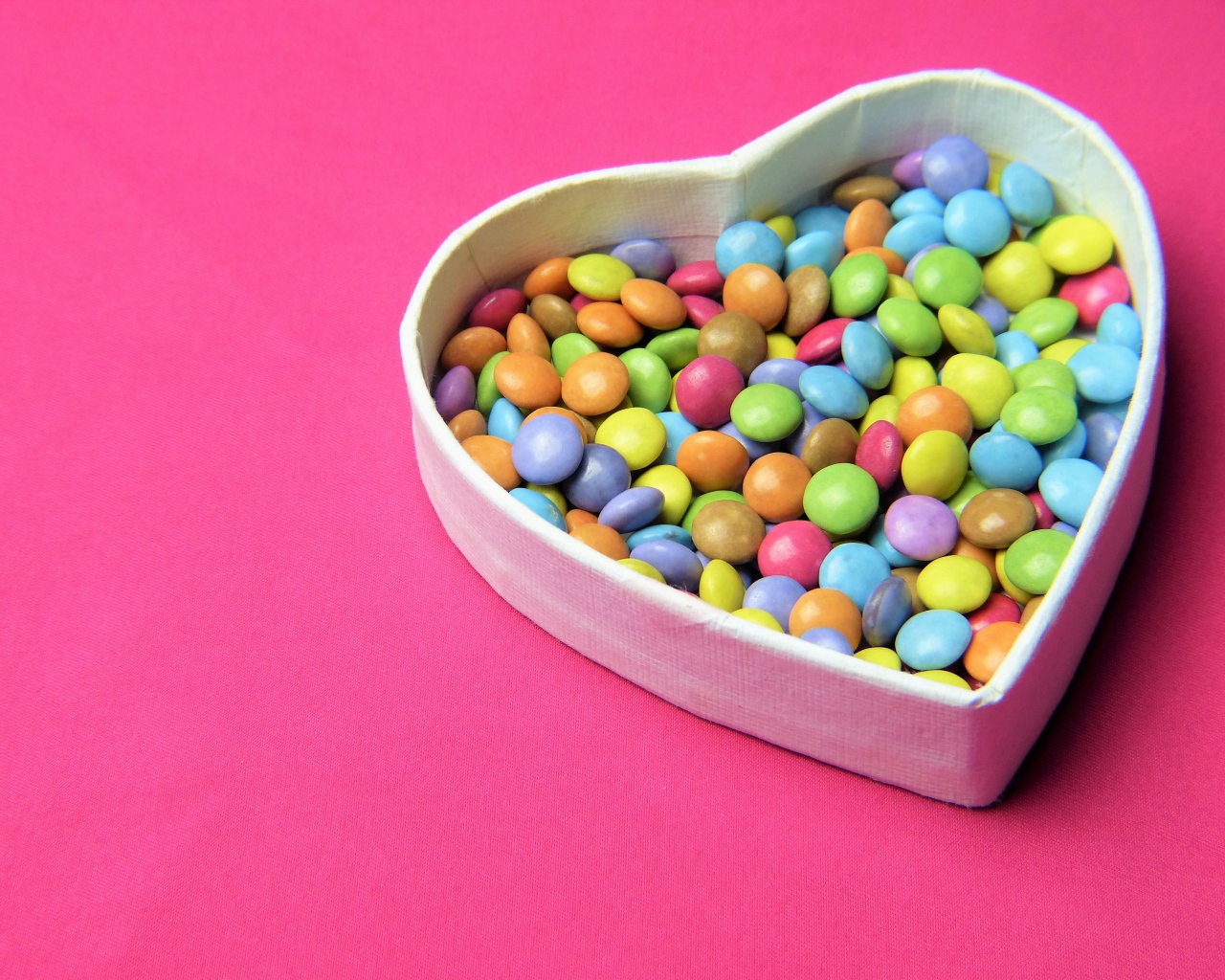 Коробка в форме сердца с разноцветными конфетами на розовом фоне