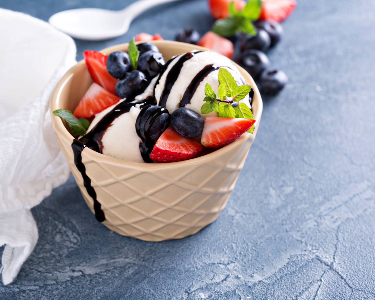 Шарики мороженого в стакане на столе с клубникой и ягодами черники