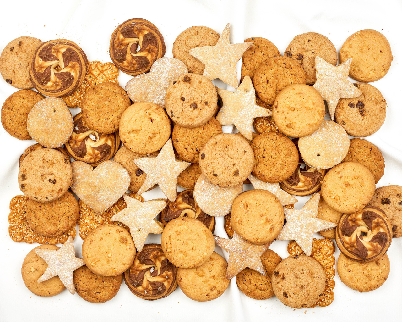 Много песочного печенья разной формы на белом фоне