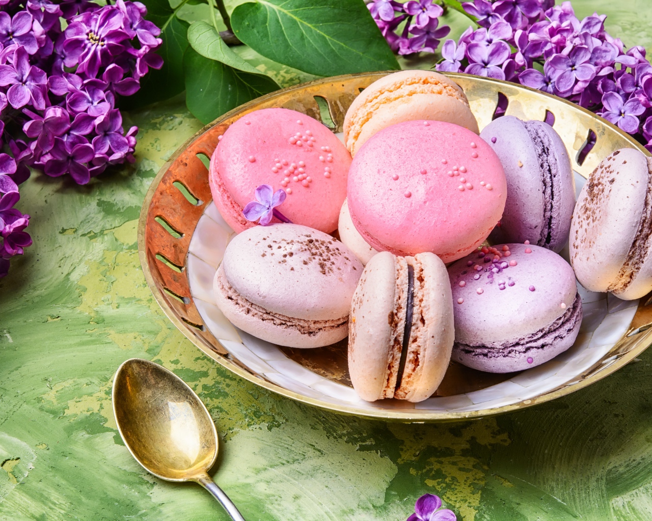 Разноцветный десерт макарон в тарелке на столе с цветами сирени 