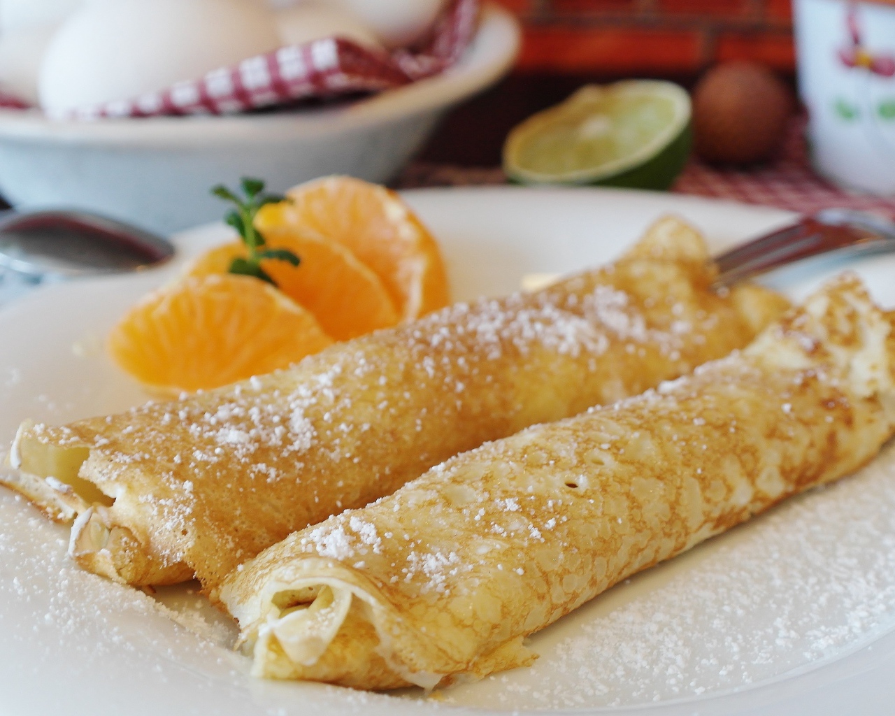 Блины с сахарной пудрой на тарелке с дольками мандарина