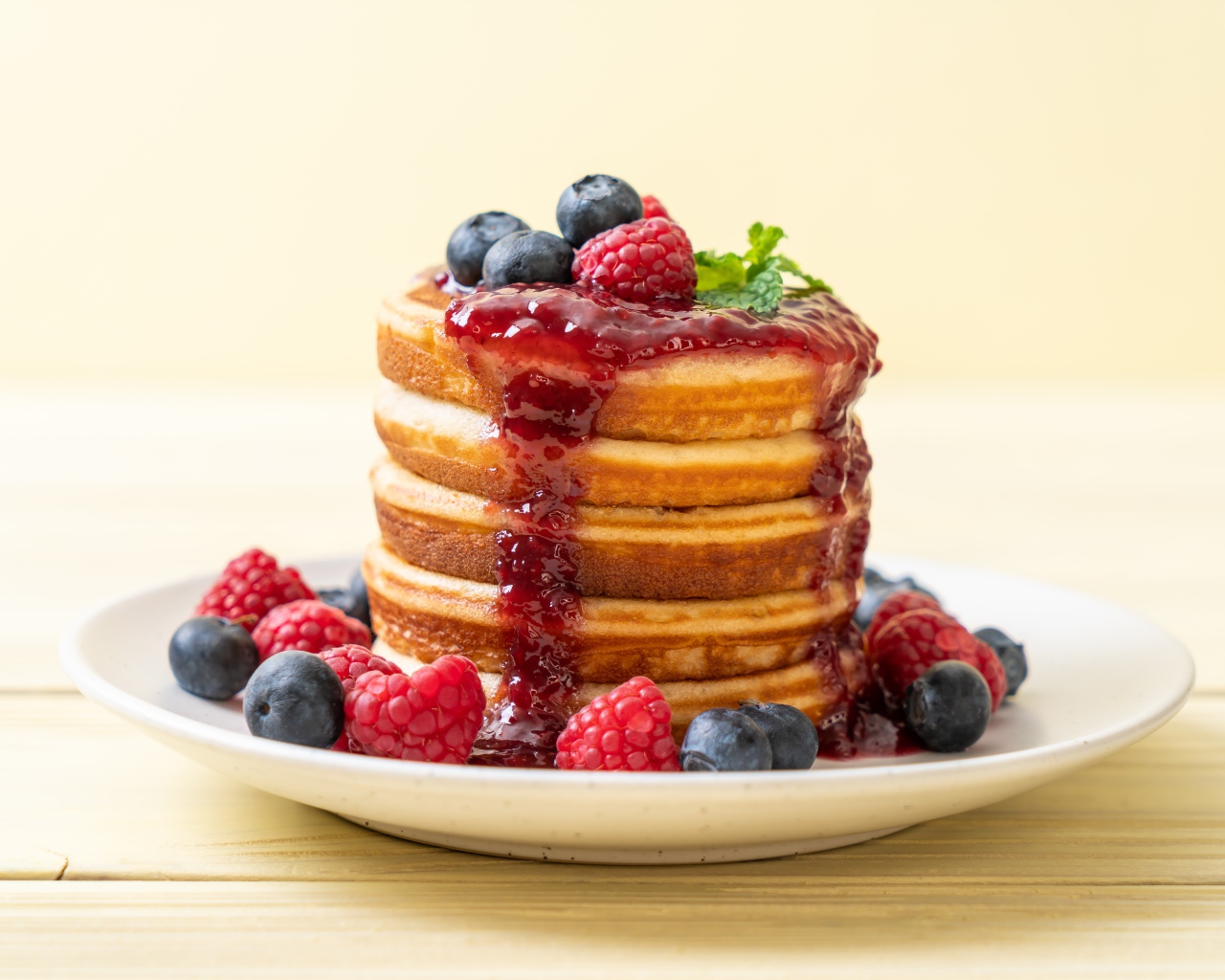 Румяные панкейки с джемом и ягодами черники и малины на тарелке