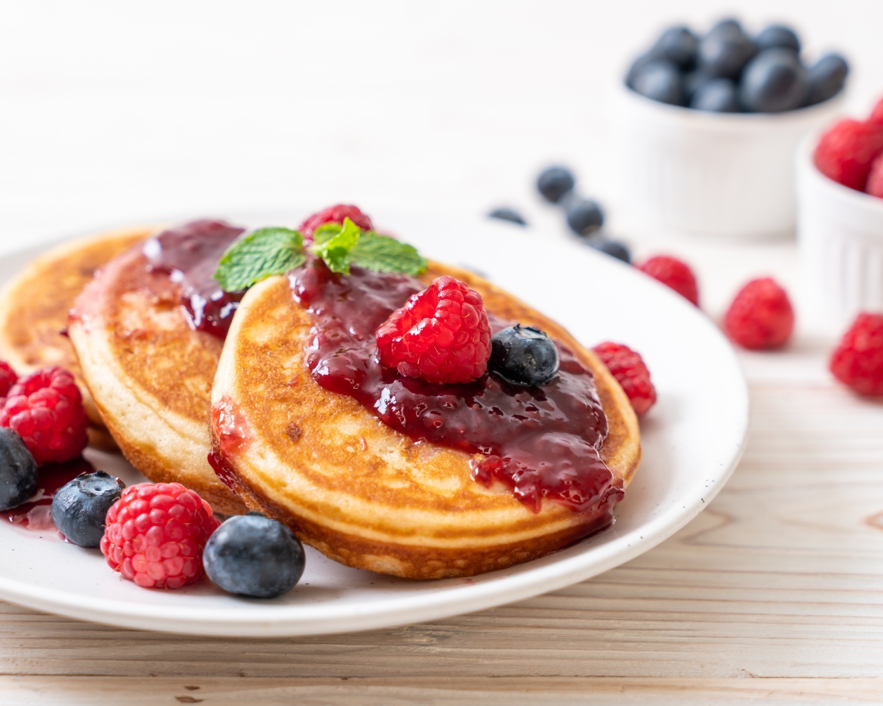 Румяные оладьи с джемом на тарелке с ягодами черники и малины
